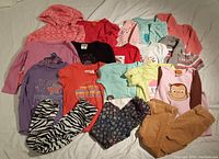 Overview of assorted girls size 5 clothing laid flat, showing various tops, pajamas, and pants of multiple colors and prints.