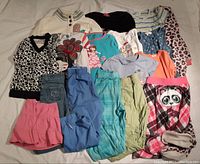 Overview of all clothing items spread out on bed showing diversity of tops, bottoms, and sleepwear