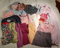 Top view of various girls size 6 clothing items including tops, leggings, a skirt, and shorts in pink, blue, and floral patterns.