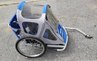 Side angled view of folding kids bike trailer showing blue and gray fabric, mesh windows, wheels, and hitch arm.