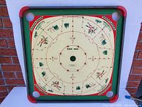 Top view of the circular game board side with Western theme featuring cowboys, horses, and trees in red and green on a cream background with four corner holes.