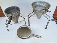 Three antique metal baking sifters with conical mesh and wire tripod legs
