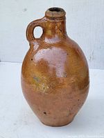 Front-left side view of the brown glazed stoneware jug showing the rounded body and intact handle.