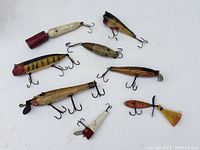 Overhead image of nine wooden fishing lures with varied colors and hooks, showing condition and makeup.