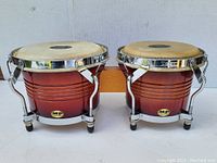 Full view of two connected Mano Percussion bongos, showing wood shells and natural drumheads with chrome tuning hardware.