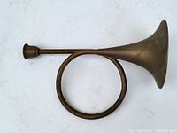 Side view of brass horn showing the circular coil, mouthpiece, and flared bell.