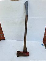 Full length view of the vintage fireman's axe, showing wooden handle and metal head with red paint.