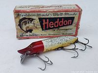 Photo showing the Heddon Vamp Spook fishing lure in front of worn original Heddon box.