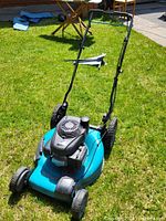 Front view of blue deck lawn mower on grass with visible pull-start gas engine and handlebar.