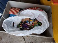 Top view of a large plastic tote containing a white plastic bag filled with assorted vintage Playmobil toy figures and accessories.