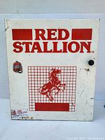 Front view of the Red Stallion automotive parts cabinet door with logo and graphics visible along with a black knob and small mounted red jacket and helmet items.