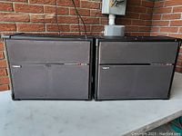Two Roland SRS-120 speakers side by side with visible front fabric covers and logos. Shows overall condition and size.