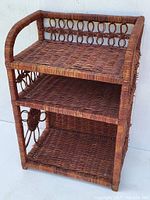 Front angled view showing the three wicker shelves and decorative loop detail on the side panel