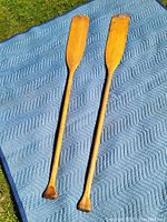 Four vintage wooden canoe paddles laid out on a blue quilted blanket outdoors showing differences in length and wear.