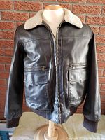 Front view of vintage Levi's men's medium leather bomber jacket on mannequin against brick wall.