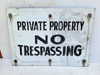 Close-up of vintage steel sign with black text on white background stating 'PRIVATE PROPERTY NO TRESPASSING' showing mounting holes and surface wear.