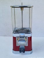 Front view of vintage red and chrome tabletop gumball machine showing coin slot and maple leaf emblem.