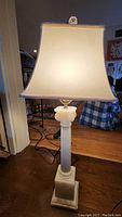 Full side view of the alabaster carved neoclassic column lamp with the white fabric shade lit, showing overall height and shape.