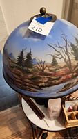 Close view of reverse-painted glass lampshade showing blue sky and tree landscape artwork