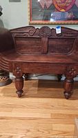 Front view of carved wood loveseat chair showing detailed carvings on seat, legs, and backrest.