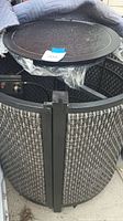 Photo showing the tall woven barrel fire pit with black metal frame and textured fire diffuser cover still in plastic.