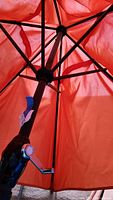 Internal structure and hand crank mechanism of one orange outdoor umbrella, showing the metal ribs and black crank handle.