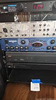 Rack-mounted units: Furman voltage meter at top, silver Focusrite channel strip, blue Behringer unit, black amplifier and empty drawer