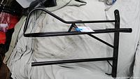 Side view of black metal saddle and blanket bar on a light cloth background showing curved top bar and support rods.