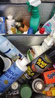 Close-up of various cleaning supplies including aerosol cans, sprays, and bottles inside a cooler bag