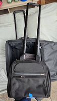 Two Tumi luggage bags, carry-on and suitcase, showing telescopic handles and exterior front pocket of carry-on.