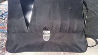Front view of the black Valextra Milano Stationery briefcase style bag showing the locking clasp and leather accent.