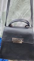 Front view of Zac Posen black leather handbag with silver tone hardware clasp and top handle