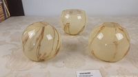Three beige glass lamp shades with brown marbling seen from above and side angle.