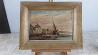 Framed oil painting showing seashore scene with boats and buildings in muted tones