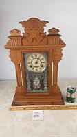 Full view front of carved Ansonia wooden mantle clock with etched glass door, showing size scale with soda can and ruler.