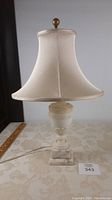 Lamp fully visible with shade off-white fabric, marble base and brass finial topped with working cord.
