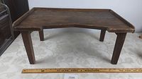 Side angle view of the antique wooden bed tray showing its four legs, the notch in the front edge, and measuring scale in front.