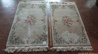 Two similar plush bedside carpets side by side, showing overall condition and size relative to floor, both with floral central design and fringed edges.