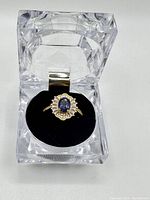 Front view of blue topaz center ring in clear acrylic box with black velvet insert.