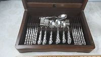 Top view of wooden chest open displaying cutlery set with knives, forks, and spoons neatly arranged.