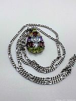 Pendant and chain arranged on flat surface, showing multi-coloured sapphires and chain detail.