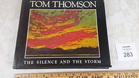 Cover of the hardcover book showing the title 'Tom Thomson' and subtitle 'The Silence and the Storm' with a colorful painting of a sunset.