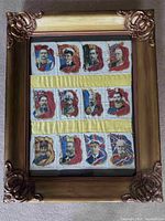 Full view of framed silk panel showing twelve WW1 portraits arranged in three rows with yellow fabric strips sewn between rows inside a gold ornate frame.