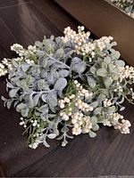 Close-up of faux floral half sphere arrangement showing frosted pebble green leaves and clusters of small off-white berries on dark wood surface.