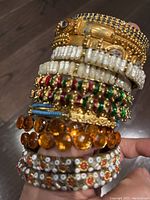 Close-up of stacked bracelets showing diverse designs including gold-tone metal, pearl-like beads, colored stones, and floral bead patterns.