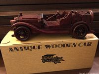 Side view of carved wooden vintage car model on original box.