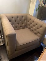 Front angle of beige upholstered armchair showing button tufting and plush cushioned seat