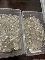 Two large plastic storage boxes filled with clear glass chandelier crystal prisms placed on dark floor.