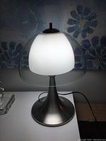 Table lamp illuminated showing the milk glass inner shade surrounded by the clear glass outer shade on a chrome base.