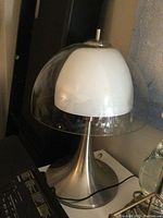 Table lamp with outer clear glass shade and inner milk glass shade on chrome base taken from an angle showing the lamp off.